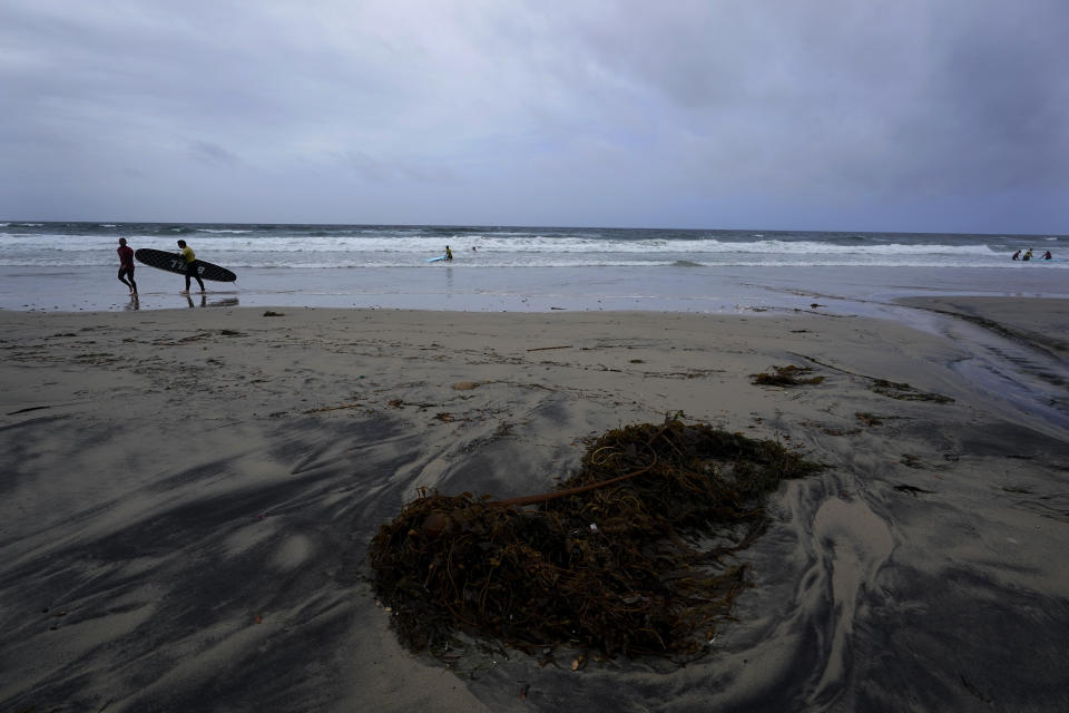 A man carries a surfboard during a surfing lesson in between rainstorms, Tuesday, March 21, 2023, in San Diego. Californians are tired. Tired of the rain, tired of the snow, tired of stormy weather and the cold, relentlessly gray skies that have clouded the Golden State nearly nonstop since late December. (AP Photo/Gregory Bull)