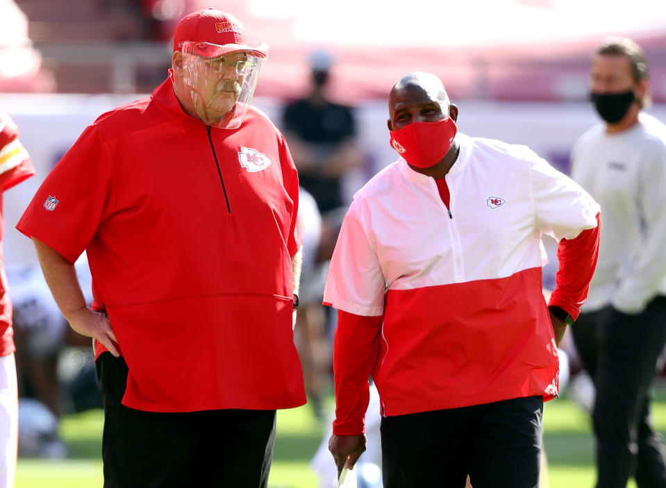 Andy Reid, wearing a face shield, speaks with offensive coordinator Eric Bieniemy, wearing a face mask.