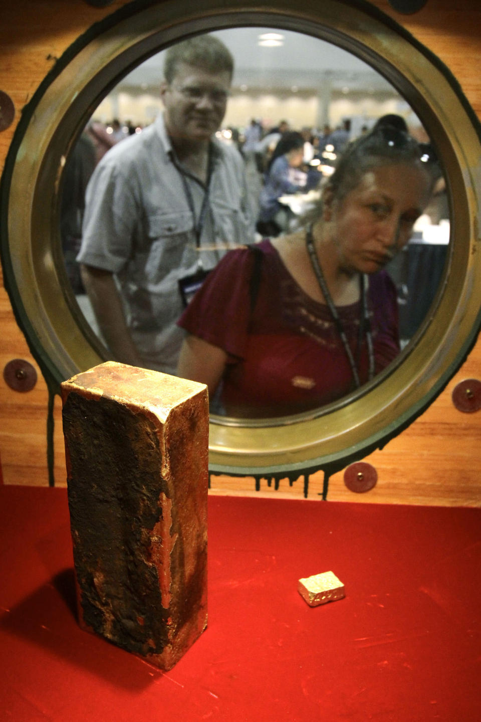 In this Aug. 10, 2010 photo, coin collector Darlene Corio, of Rochester, N.Y., right, peers through a circular window at a gold ingot weighing more than 662 ounces as her husband, Tim Corio, left, looks on at a display at the World's Fair of Money in Boston. The ingot was among two tons of California Gold Rush gold recovered from the shipwreck of the S.S. Central America which sank in 1857. (AP Photo/Steven Senne)