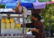 A masked fruit vendor prepares her streetside cart while waiting for customers near downtown Los Angeles on Wednesday, Aug. 5, 2020. California lawmakers are considering requiring employers to notify workers and public health officials about positive COVID-19 cases in the workplace. Violators could be charged with a misdemeanor and assessed a fine of up to $10,000. Supporters say the bill is necessary to protect workers. But business groups say the bill is so vague it will be impossible to comply with. (AP Photo/Richard Vogel)