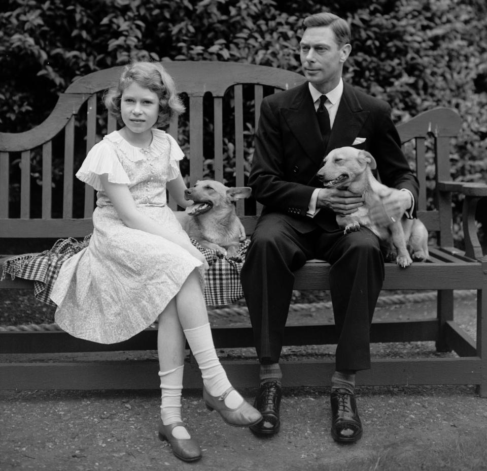 July 1936: George, Duke of York and Princess Elizabeth sitting on a bench with their corgi dogs in the grounds of their London home, 145 Piccadilly. (Photo by Lisa Sheridan/Studio Lisa/Getty Images)