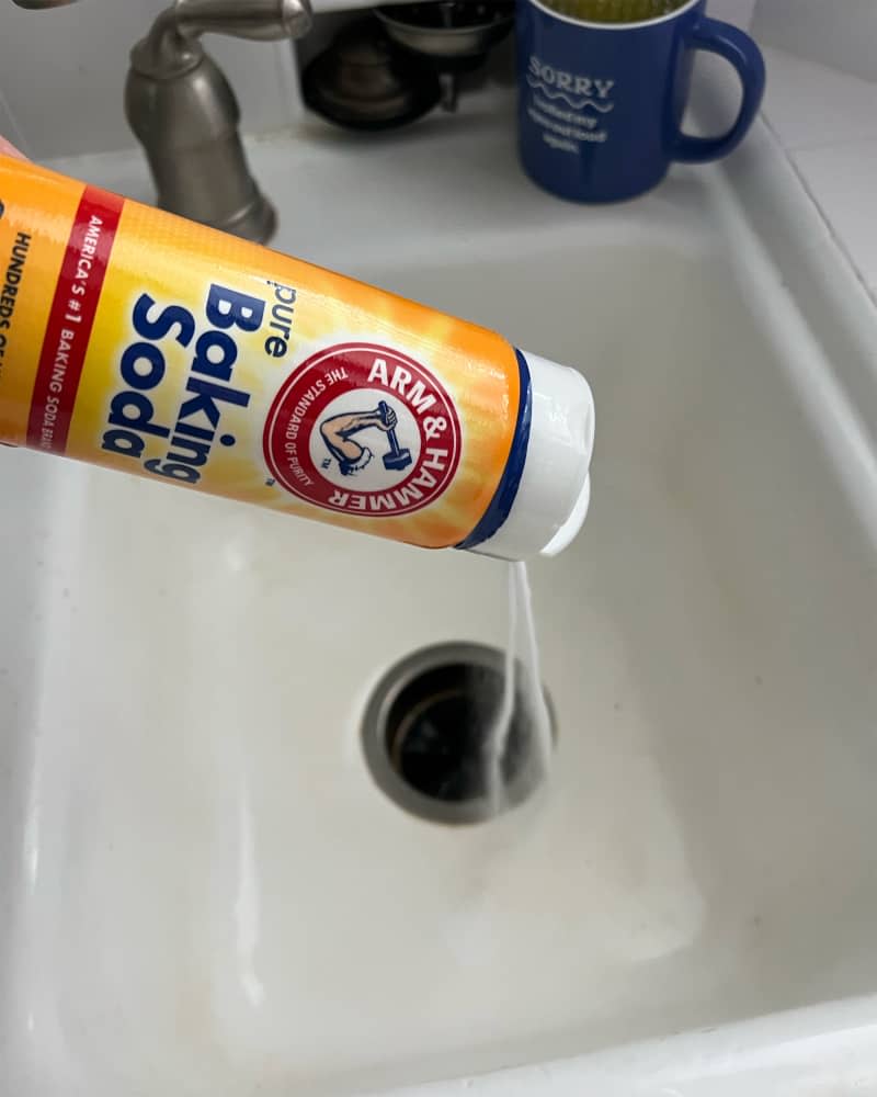 Someone sprinkling baking soda into sink.