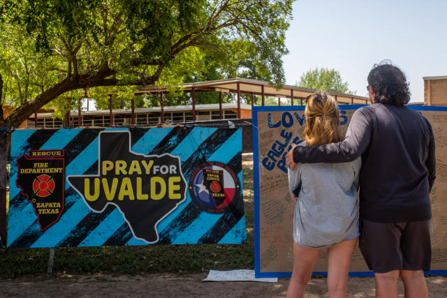 A man and a woman look at a mural that shows and outline of the state of Texas and reads: Pray for Uvalde.