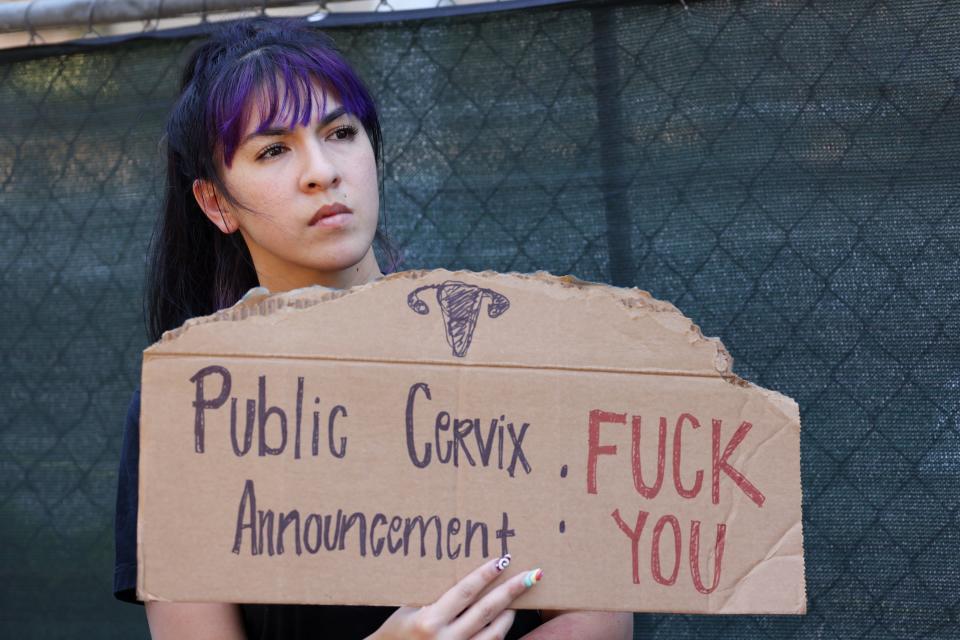 A woman holds a sign "Public Cervix Announcement."