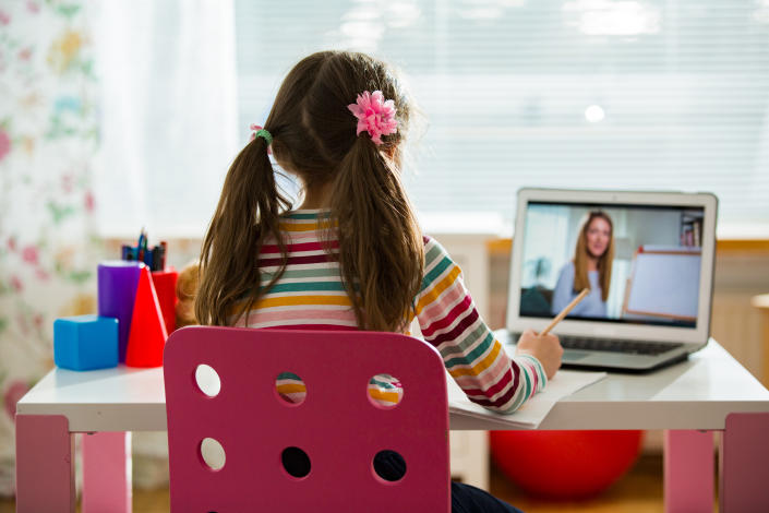 A young girl sits at a desk participating in a video call with her teacher on a laptop.  (Getty Images)