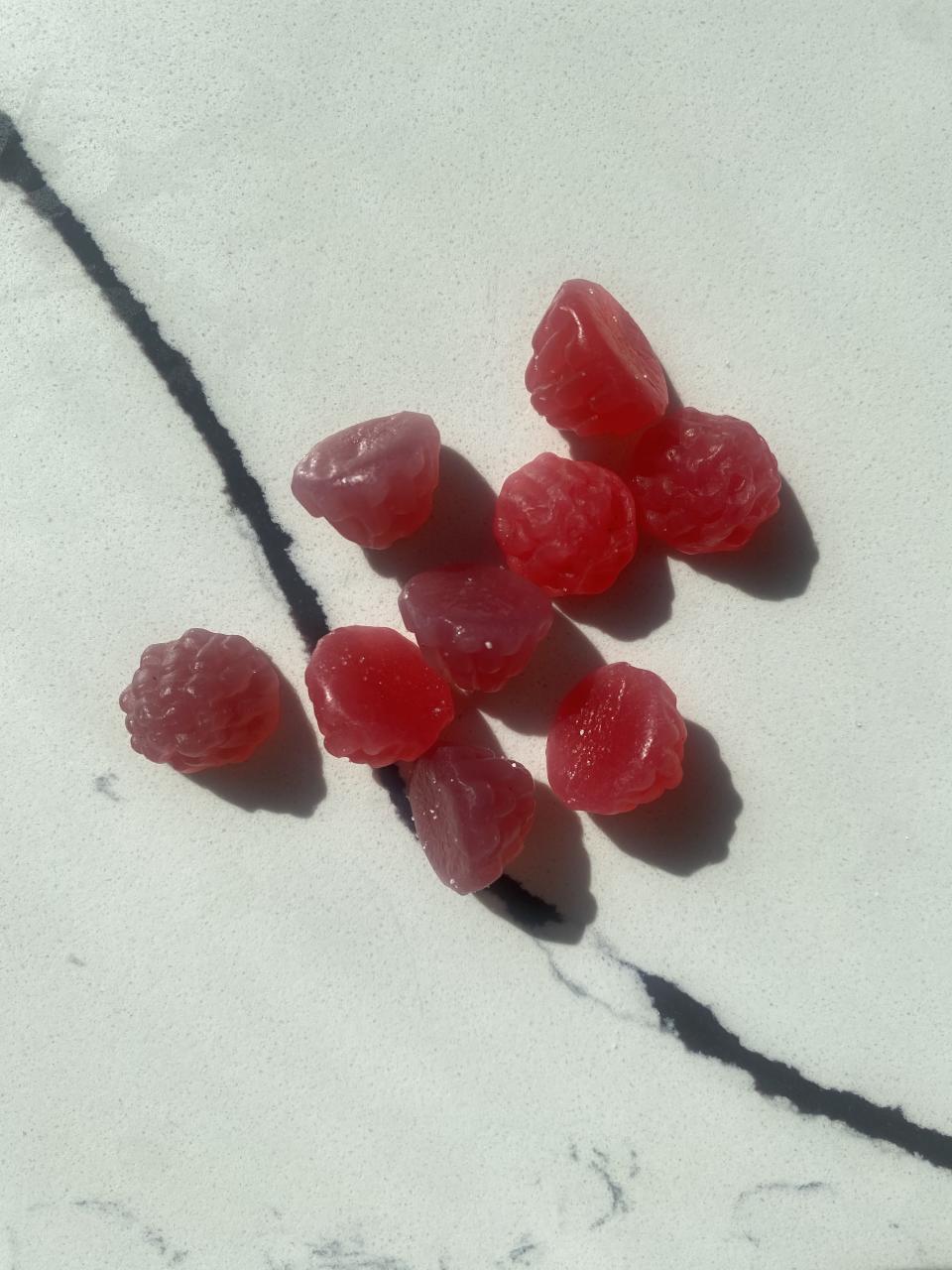 A group of raspberry-shaped gummy candies is spread out on a marble-patterned surface