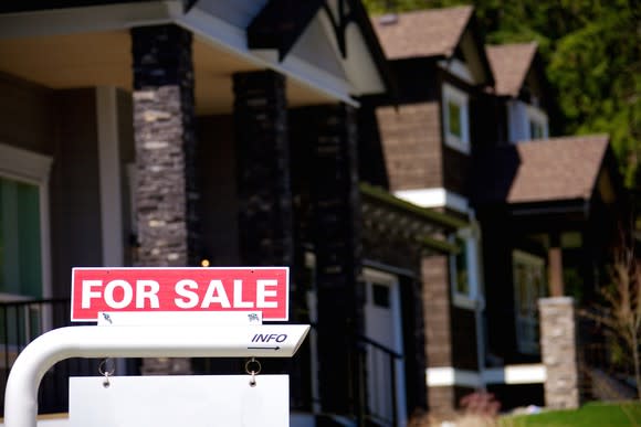 A for sale sign in front of several houses in background.