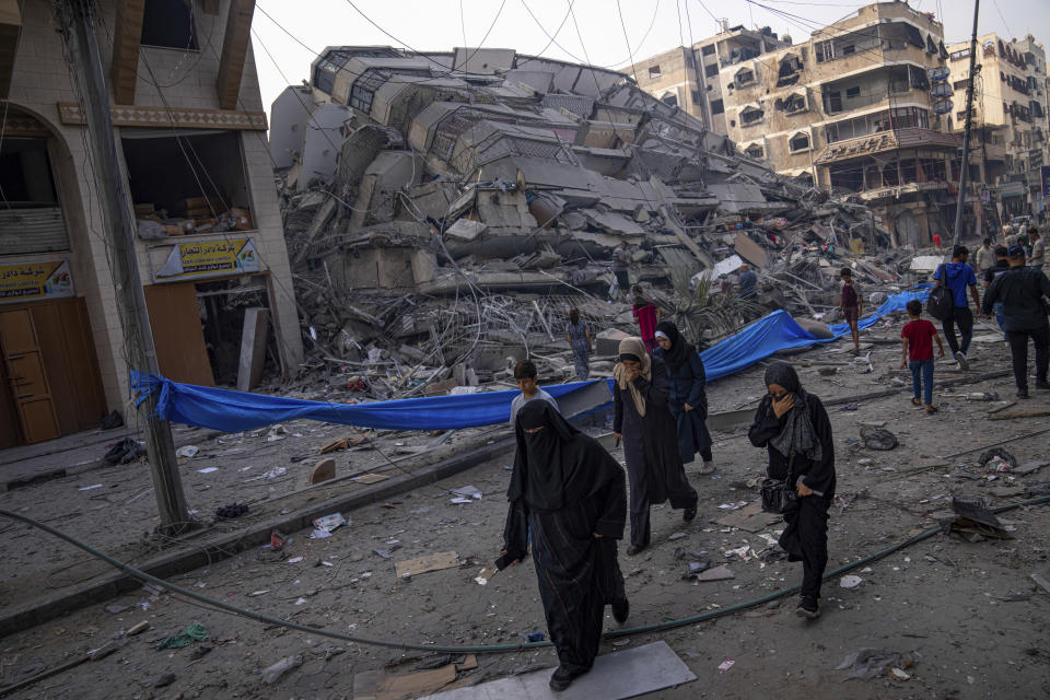 Palestinians walk by the rubble of a building after it was struck by an Israeli airstrike, in Gaza City, Sunday, Oct. 8, 2023. The militant Hamas rulers of the Gaza Strip carried out an unprecedented, multi-front attack on Israel at daybreak Saturday, firing thousands of rockets as dozens of Hamas fighters infiltrated the heavily fortified border in several locations by air, land, and sea, killing hundreds and taking captives. Palestinian health officials reported scores of deaths from Israeli airstrikes in Gaza. (AP Photo/Fatima Shbair)