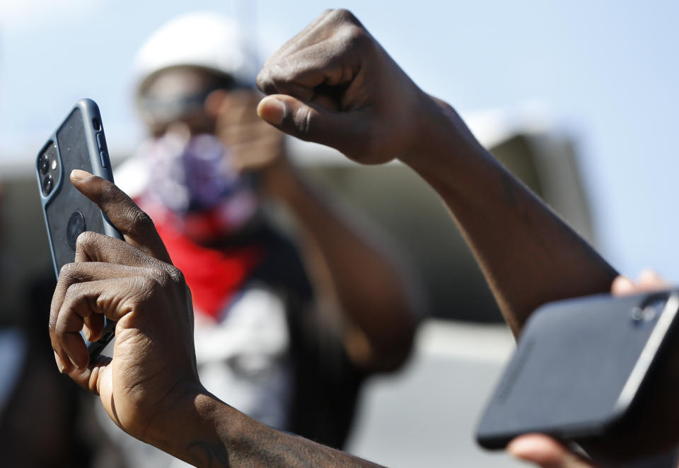 A protester raises his fists as he films and photographs the crowd and speakers during a Caribbean-led Black Lives Matter rally at Brooklyn's Grand Army Plaza, Sunday, June 14, 2020, in New York. (AP Photo/Kathy Willens)