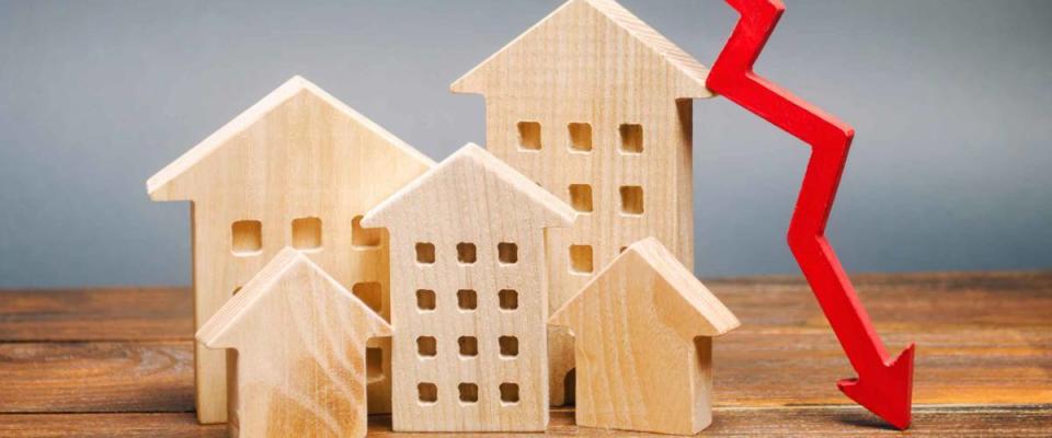 Miniature wooden houses and a red arrow down. The concept of falling mortgage rates