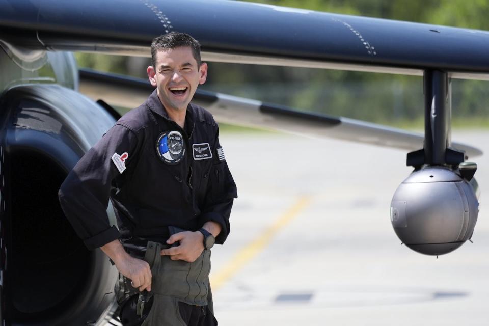 A man in a black shirt stands in front of a plane.