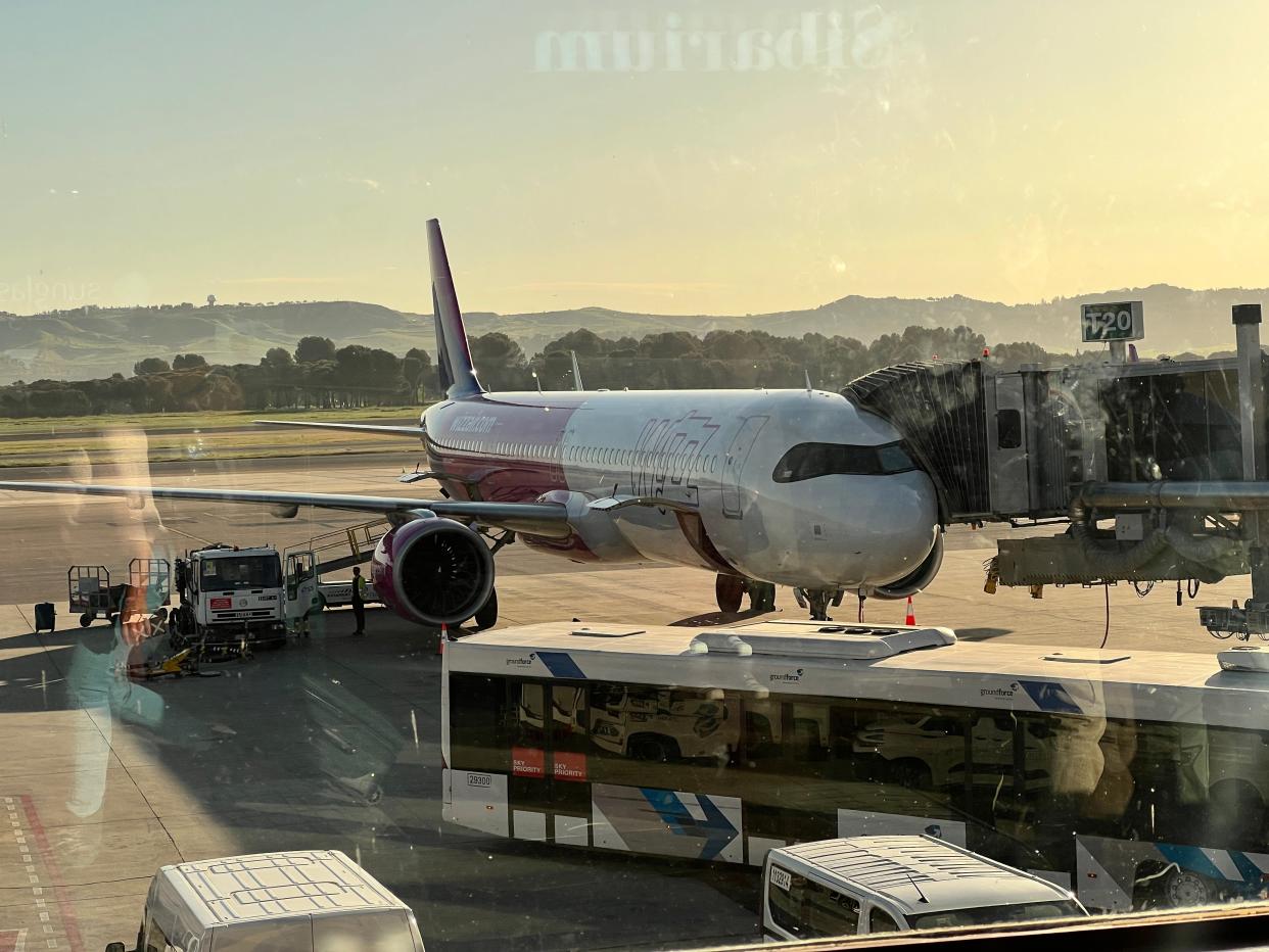 A Wizz Air A321neo parked at the gate next to a jetbridge at Madrid Airport during a sunrise.