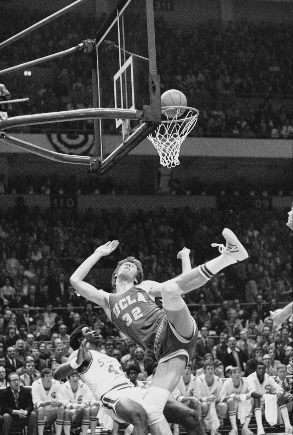 FILE - UCLA's Bill Walton (32) falls over North Carolina State's David Thompson during the first period of the NCAA semifinals at Greensboro, N.C., March 23, 1974. (AP Photo/File)