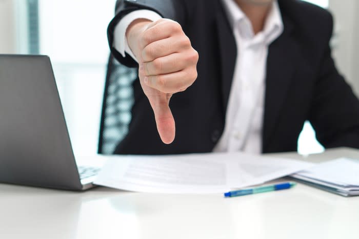 Businessman sitting in front of a laptop and making the thumbs down gesture with his right hand.