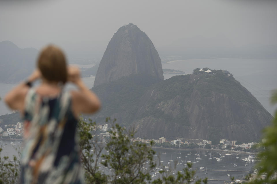 A tourist takes a picture of the Sugar Loaf mountain, in Rio de Janeiro, Brazil, Tuesday, March 17, 2020. The company that administers transport and installations at Rio's Sugarloaf Mountain, another postcard destination that sees 1.5 million visitors annually, said it is closing shop on Tuesday for 15 days as a measure to prevent the spread of the new coronavirus. (AP Photo/Silvia Izquierdo)