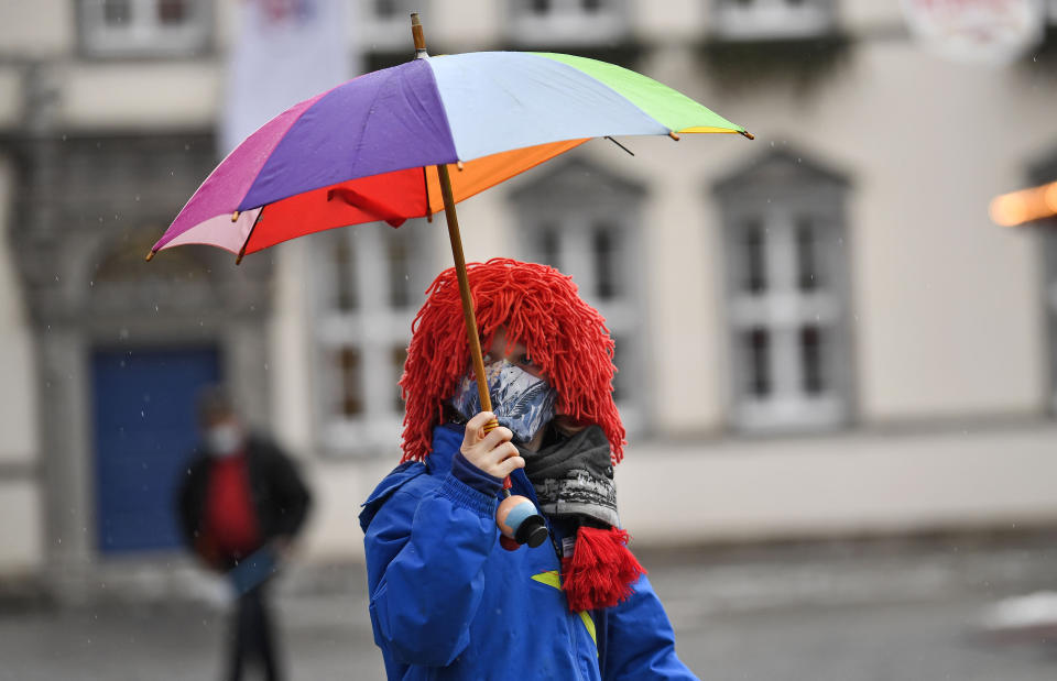 A young carnival reveller dressed as a clown holds an umbrella in the empty old town in Duesseldorf, Germany, Monday, Feb. 15, 2021. Because of the coronavirus pandemic the traditional; carnival parades are canceled but eight floats are pulled through the empty streets in Duesseldorf, where normally hundreds of thousands of people would celebrate the street carnival. (AP Photo/Martin Meissner)