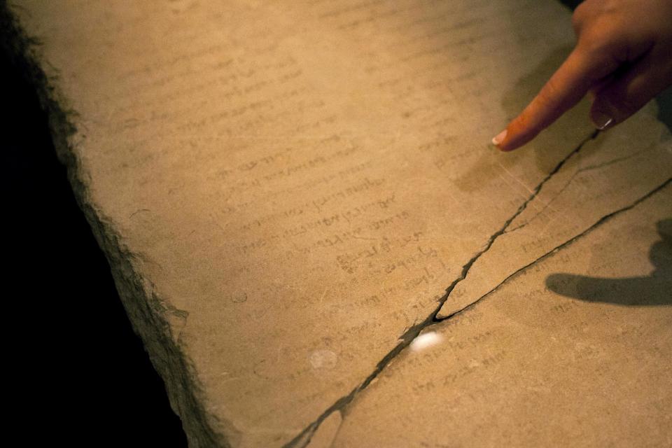 A museum worker points at the 'Gabriel Stone' as it is displayed at an exhibition at the Israel Museum in Jerusalem, Tuesday, April 30, 2013. An ancient stone with mysterious Hebrew writing and featuring the archangel Gabriel is being displayed in Israel, even as scholars continue to argue about what the inscription means. (AP Photo/Sebastian Scheiner)