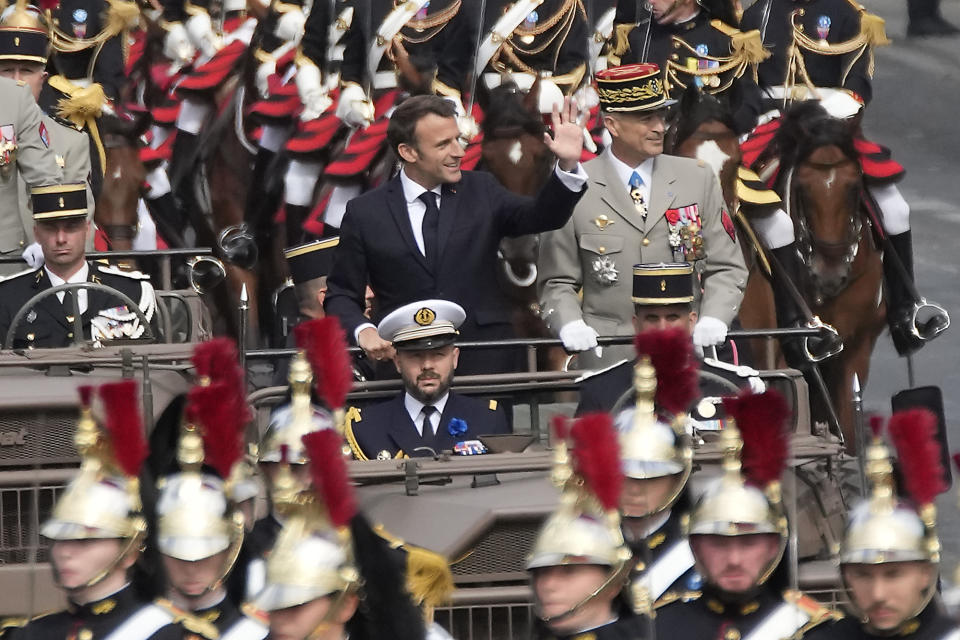 El presidente francés Emmanuel Macron saluda a los espectadores mientras asiste con el jefe del Estado Mayor, general Thierry Burkhard, al desfile del Día de la Bastilla en la avenida Champs-Elysées, París, viernes 14 de julio de 2023. (AP foto/Christophe Ena)