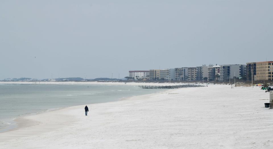 A solitary beachgoer braves Friday morning's cold weather to walk along an empty Okaloosa Island.