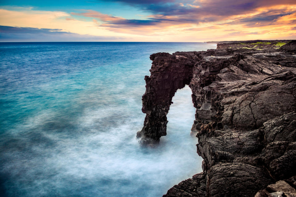 Waves crash around a rocky arch that juts out from the Hawai'i Volcanoes National Park.