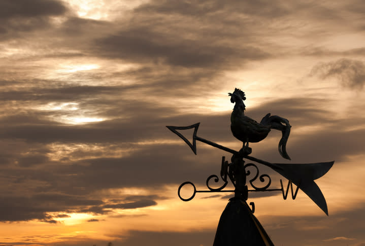 A wind vane topped with a rooster, silhouetted against a twilight sky