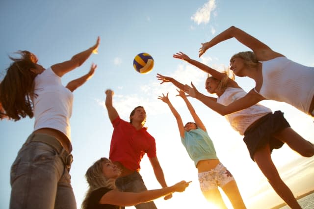 group of young people playing volleyball on the beach