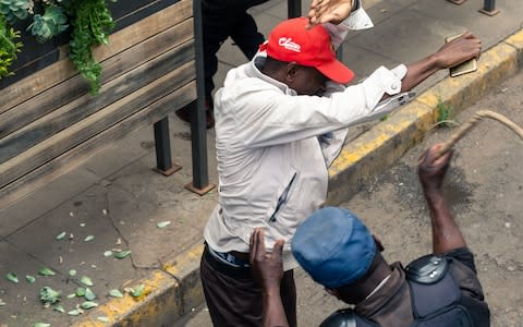 An anti-riot police man in Zimbabwe beats a man in late November - Credit: JEKESAI NJIKIZANA/AFP via Getty Images