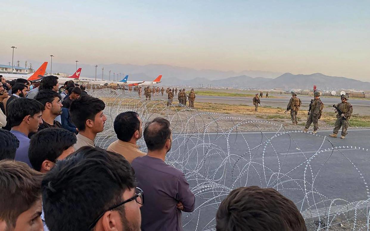 Afghans gather at Hamid Karzai International Airport in Kabul on Monday as US soldiers stand guard - Shakib Rahmani/AFP/Getty Images