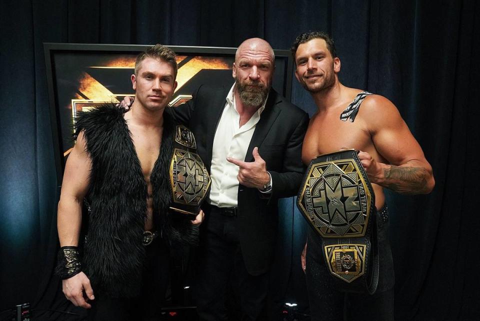 Paul “Triple H” Levesque (middle), the leader of WWE’s NXT, congratulates Breezango (Tyler Breeze, left, and Fandango) after winning the NXT tag team titles.