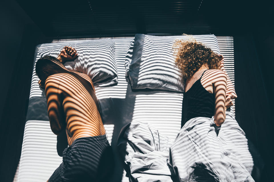 a couple sleeping in the same bed but facing away from one another and maintaining space between them