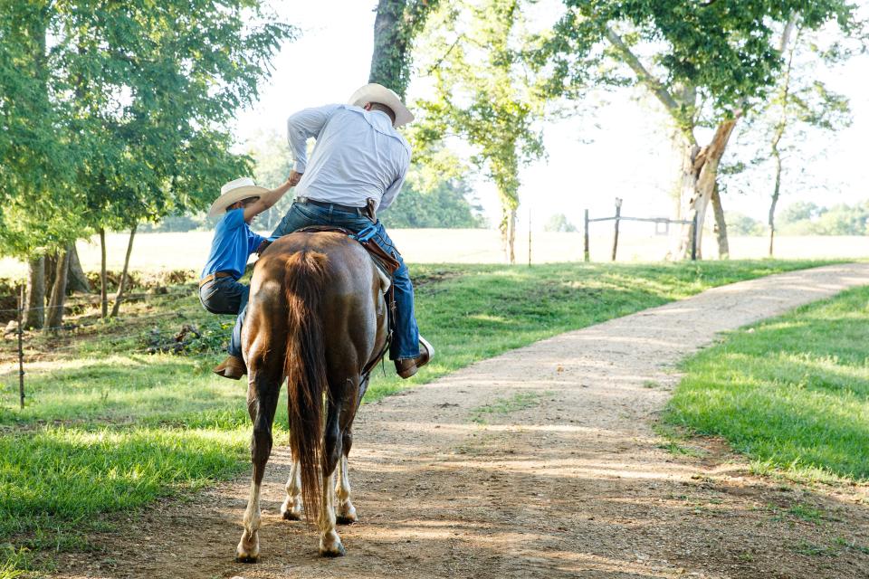 Trevor Pennington helps his son Beau (7) to get up on the family horse, Socks, after herding cattle at 1822 Farms in Williamsport, Tenn. on Monday, July 10, 2023. 