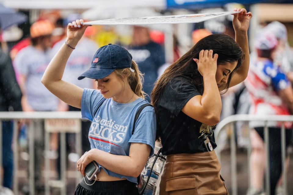 Two women hold a sign over their heads in the rain