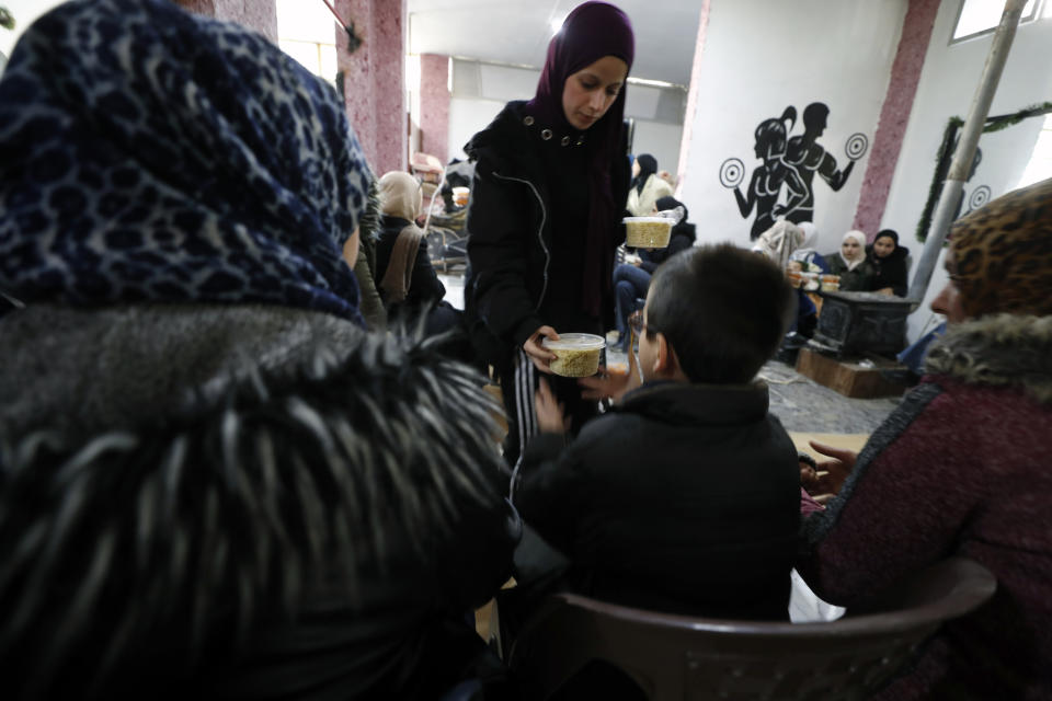 A volunteer woman distributes meals to displaced people following a devastating earthquake, in the coastal city of Latakia, Syria, Friday, Feb. 10, 2023. The 7.8 magnitude earthquake that hit Turkey and Syria, killing more than 23,000 this week has displaced millions of people in war-torn Syria. The country's 12-year-old uprising turned civil war had already displaced half the country's pre-war population of 23 million before the earthquake. (AP Photo/Omar Sanadiki)