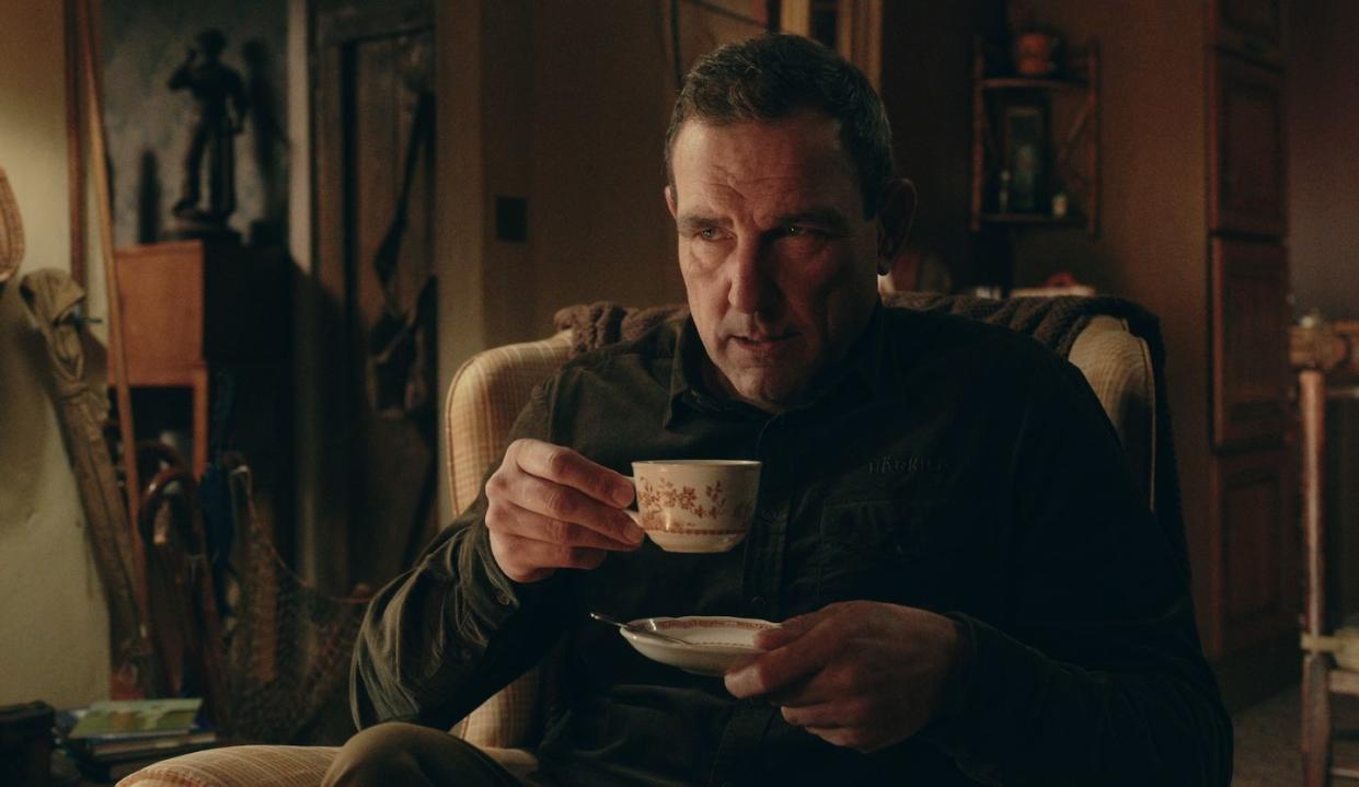 vinnie jones in the gentlemen, a man sits in a chair holding a cup and saucer