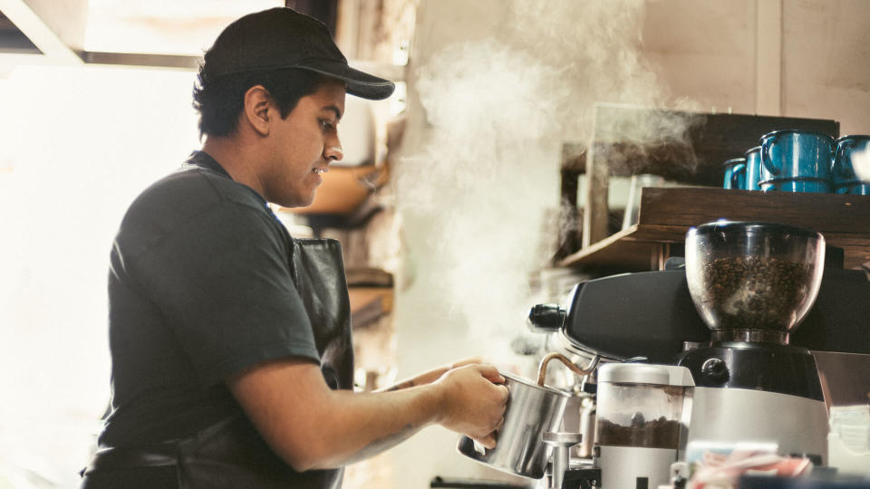Mexican Barista warming milk with a Coffee Seamer in Coffeeshop.