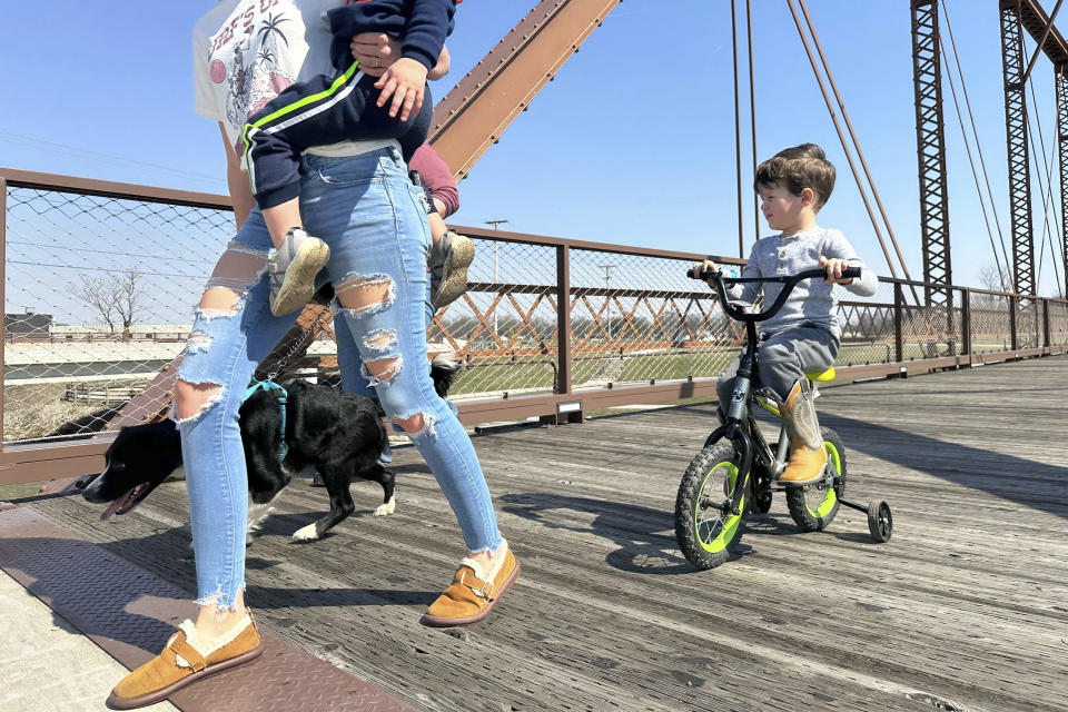 Four-year old Maxton Mercer, far right, rides his tricycle across the Kitselman bridge connecting the Cardinal and White River Greenway trails in Muncie, Ind. along with family and friends Wednesday, March 13, 2024. The Cardinal Greenways pathway born from eastern Indiana's abandoned railroad tracks will become a central cog in the Great American Rail Trail — a planned 3,700-mile network of uninterrupted trails spanning from Washington state to Washington, D.C. (AP Photo/Isabella Volmert)