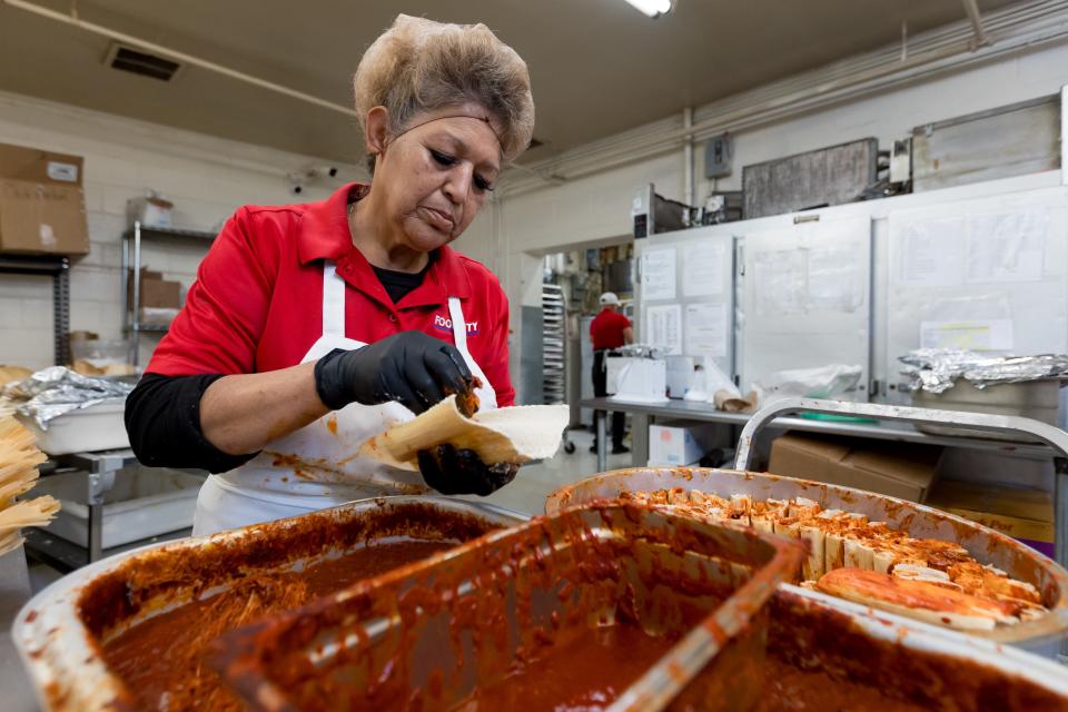 Nilfa Farfan, an employee at Food City Supermarket in El Paso, adds red chile covered pork to the center of the masa for the tamales on Tuesday, Dec. 19, 2023.