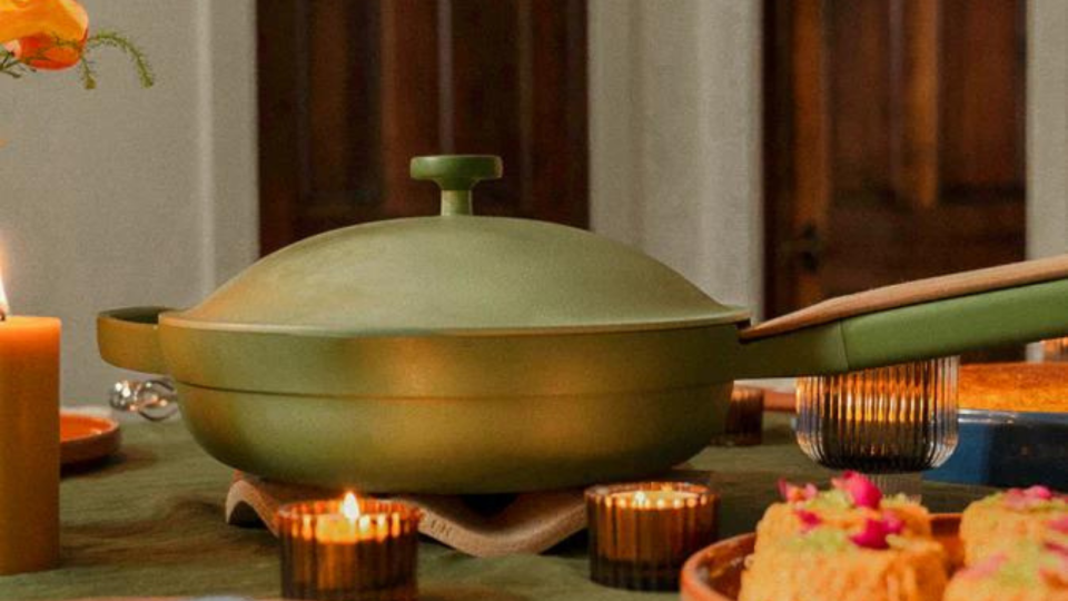 the green Always Pan, with a wooden spatula resting on its handle, on a table with candles and food