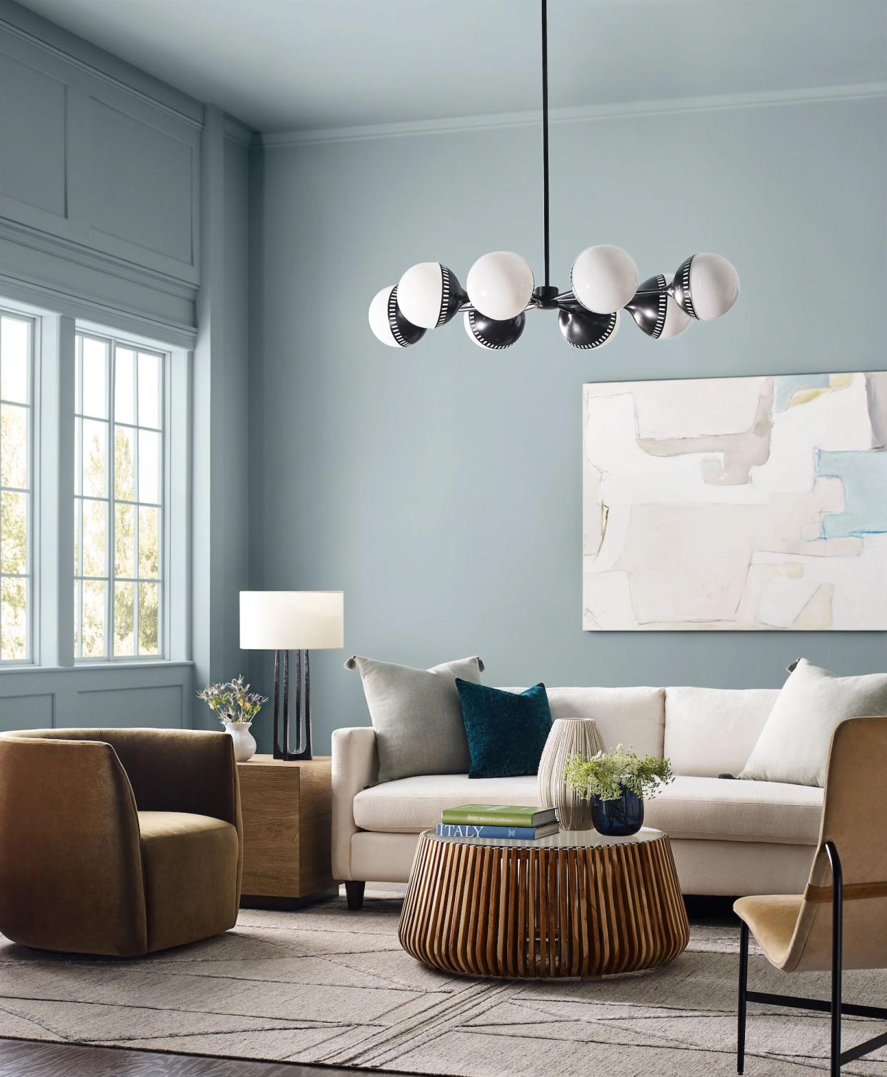  Tall light blue painted walls with wall molding around the window, a cream sofa and statement modern black chandelier. 