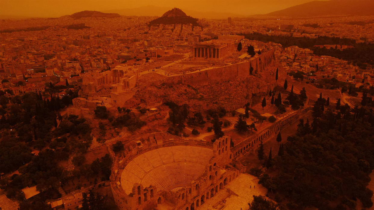  A view of Greek ruins, including the Parthenon, with a reddish haze from a dust storm. 