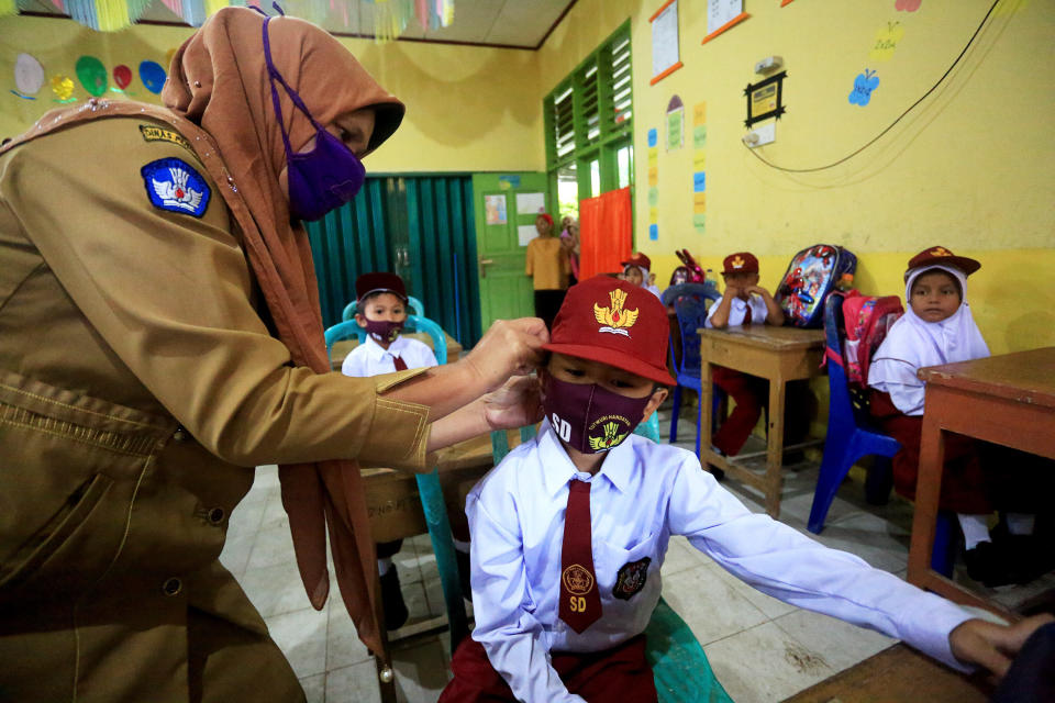 A teacher helps an elementary school student with a face mask on the first day of school in the 2020-2021 academic year in Pesisir Selatan region, West Sumatra, Indonesia, on July 13. Students in Indonesia went back to schools in low-risk areas under tight health protocols.