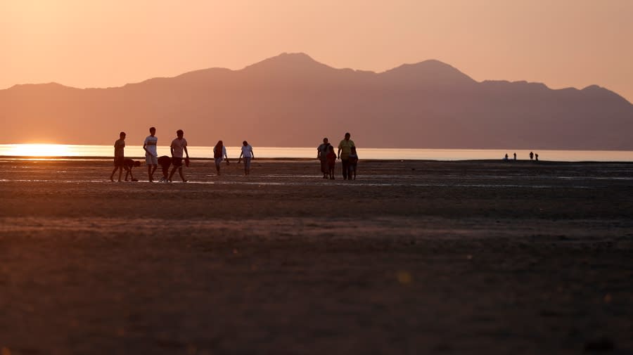 People walk on a dry section of the Great Salt Lake at sunset