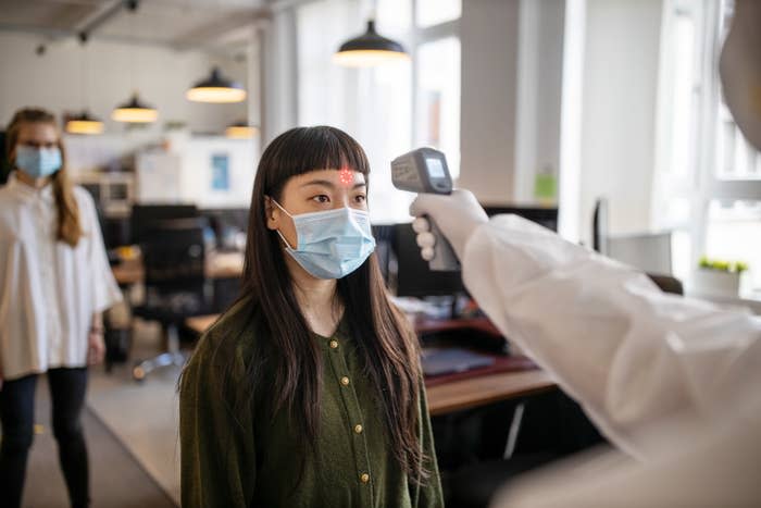 Woman wearing protective mask goes through a temperature checks before going to work in the office.