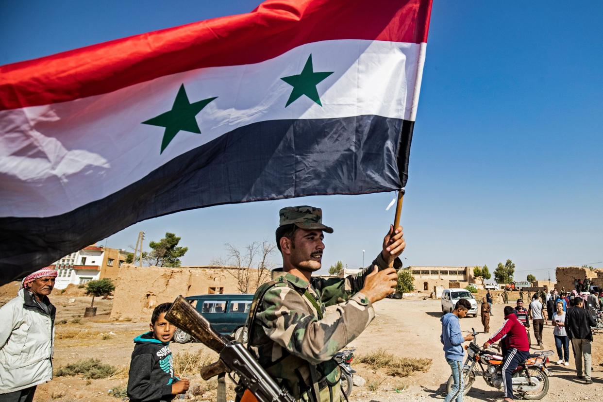 A Syrian regime soldier waves the national flag a street on the western entrance of the town of Tal Tamr in the countryside of Syria's northeastern Hasakeh province: DELIL SOULEIMAN/AFP via Getty Images