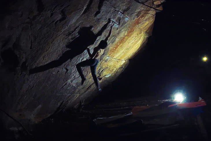 Noah Wheeler campusing the crux move of Defying Gravity, climbing in the dark with lamps.
