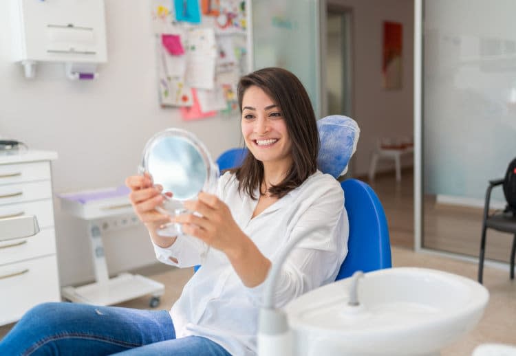Mujer joven en la consulta del dentista se mira los dientes en un espejo