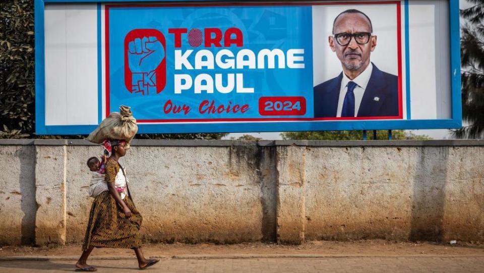     A woman carrying her baby on her back walks past an election billboard asking to vote for the current president of Rwanda and the presidential candidate of the Rwandan Patriotic Front (RPF), Paul Kagame, in Kigali on July 11, 2024