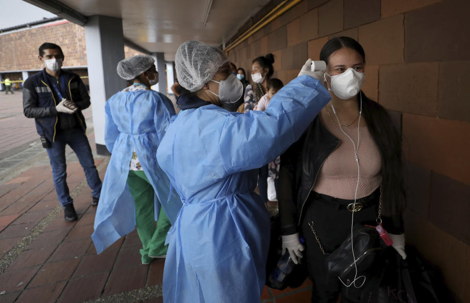 A nurse takes the temperature of a woman, outside the main bus terminal in Bogota, Colombia, Tuesday, March 24, 2020. The government announced a nationwide lockdown starting Tuesday to fight the spread of new coronavirus, putting strict restrictions on residents' movements, but emphasized it will guarantee the continuation of local agriculture and food distribution. (AP Photo/Fernando Vergara)