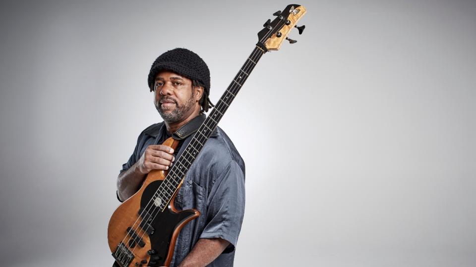 Victor Wooten holds his bass guitar with a fretwrap on the headstock