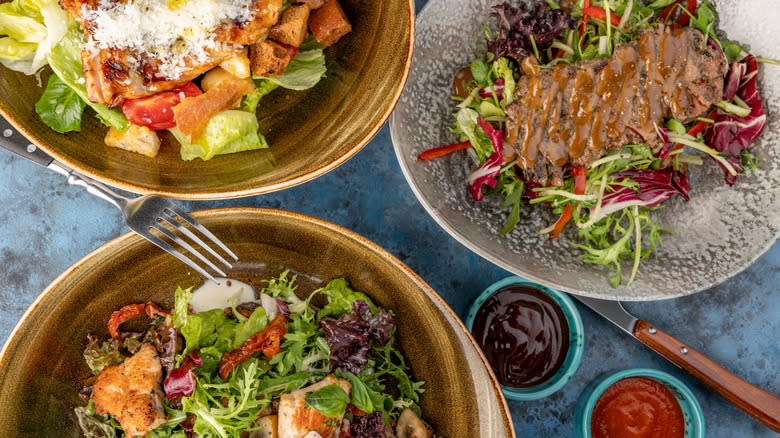 three bowls of salad and dressing cups